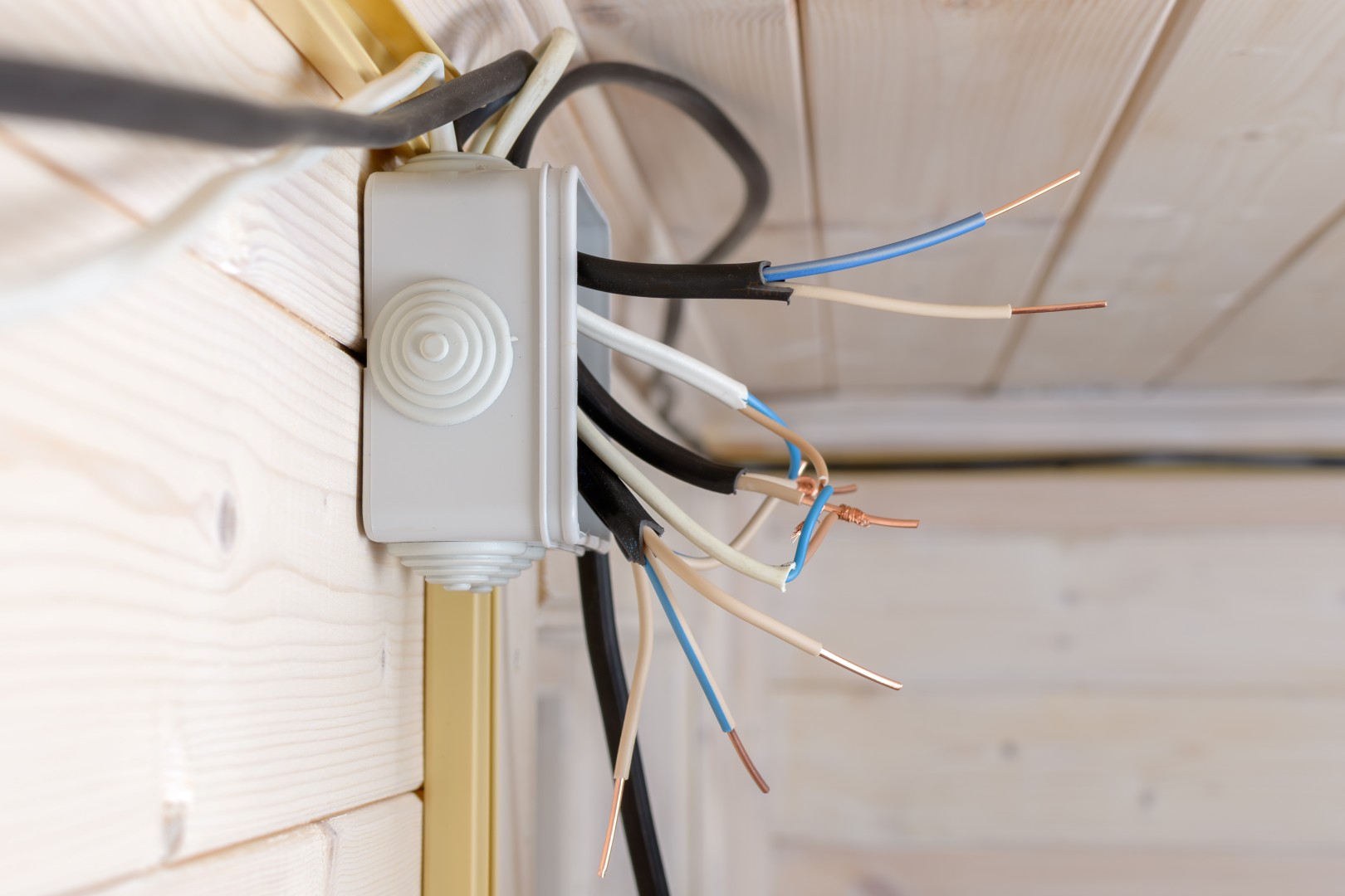 Side view of distribution box with tangled exposed wires showing stage of electrical installation on light wooden wall in house.